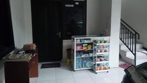 A room with a black door labeled "PENJAGA," a small shelf with various items, a wooden cabinet, and a staircase. - Jj House Kost Exclusive Nologaten (Depok)