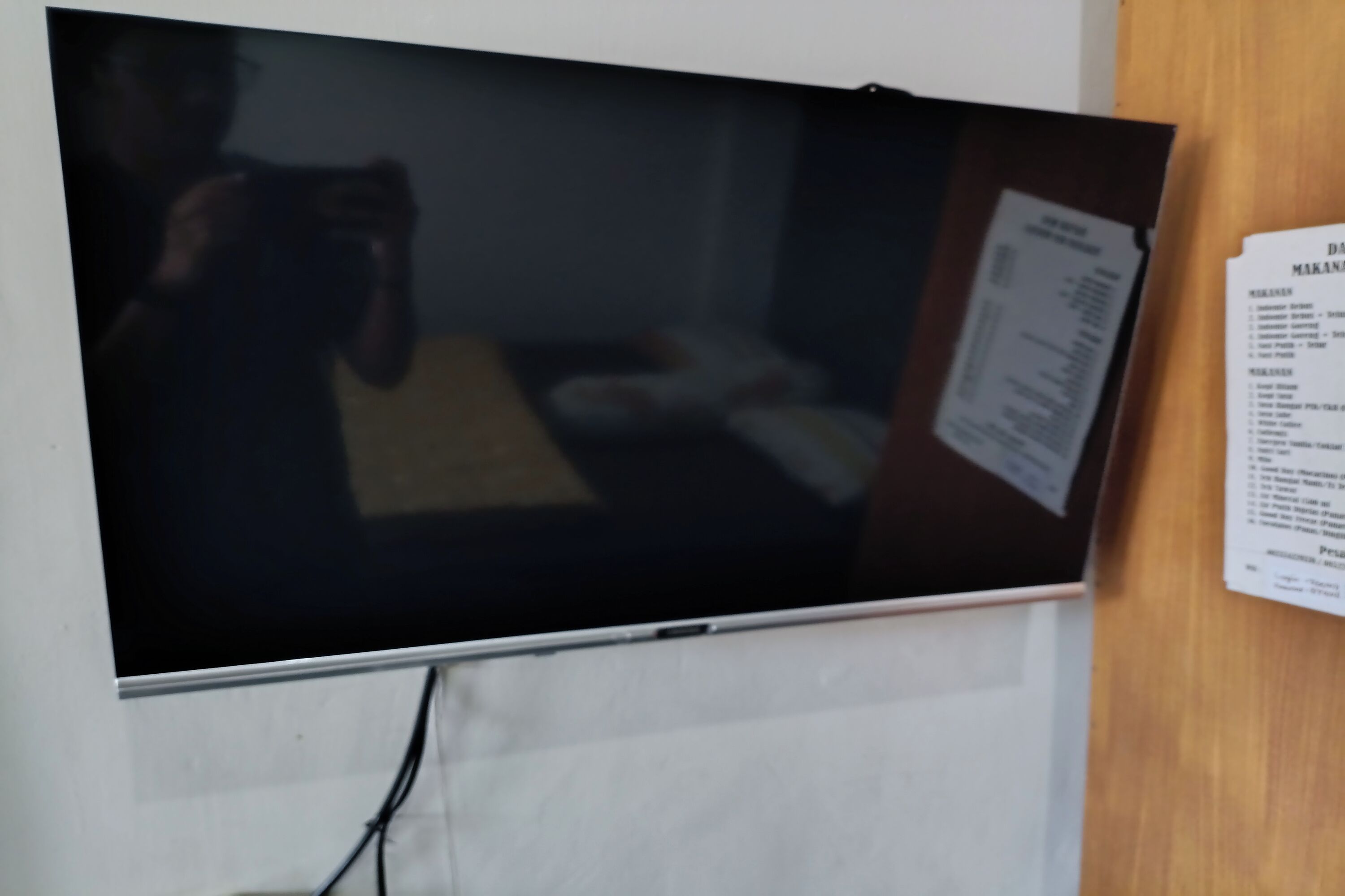 A flat-screen TV mounted on a wall, a menu board to the right, and a power cord running to the TV.