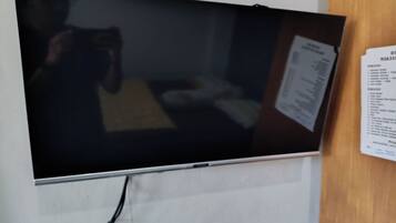 A flat-screen TV mounted on a wall, a menu board to the right, and a power cord running to the TV.