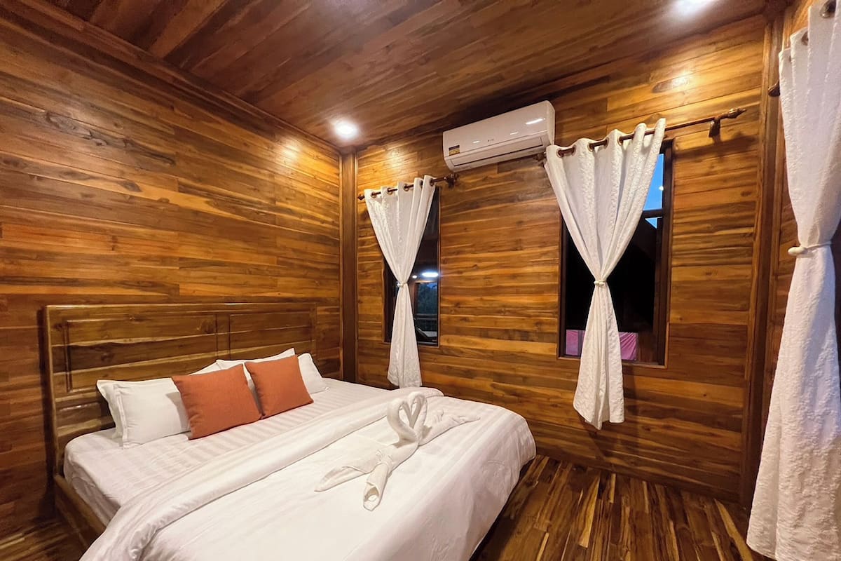 A wooden-paneled room with a bed, white curtains, and an air conditioning unit.