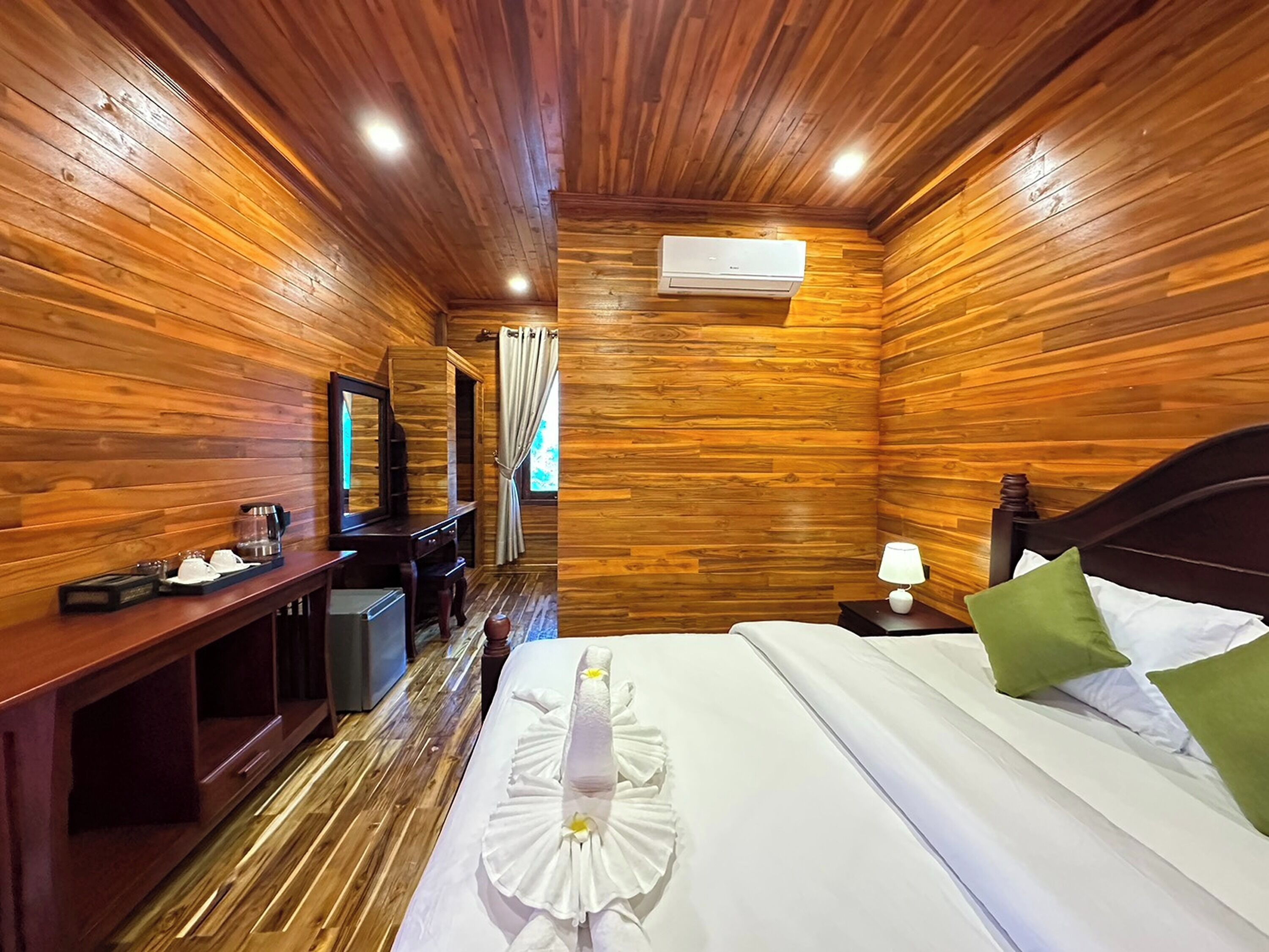 A wooden-paneled room with a bed, a desk, a mirror, and an air conditioning unit.