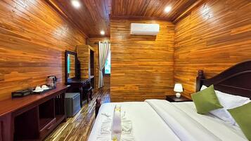A wooden-paneled room with a bed, a desk, a mirror, and an air conditioning unit.