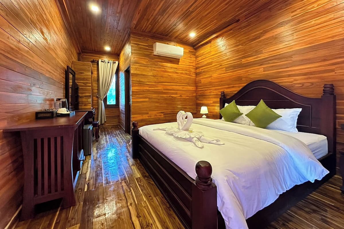 A wooden cabin-style room with a bed, a nightstand, a mirror, and a window with curtains.