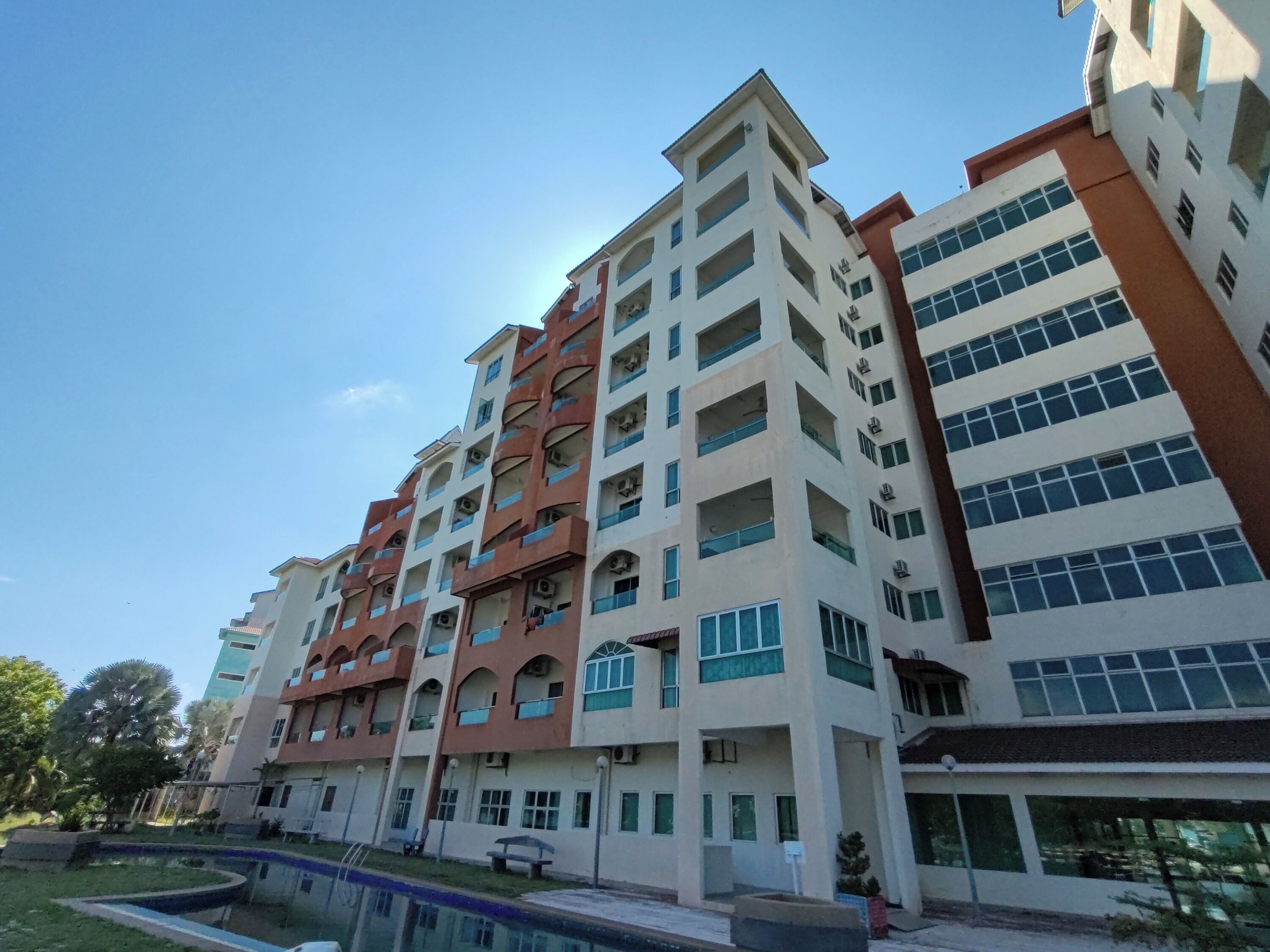 Un edificio residencial de varios pisos con balcones, piscina y césped cuidado.