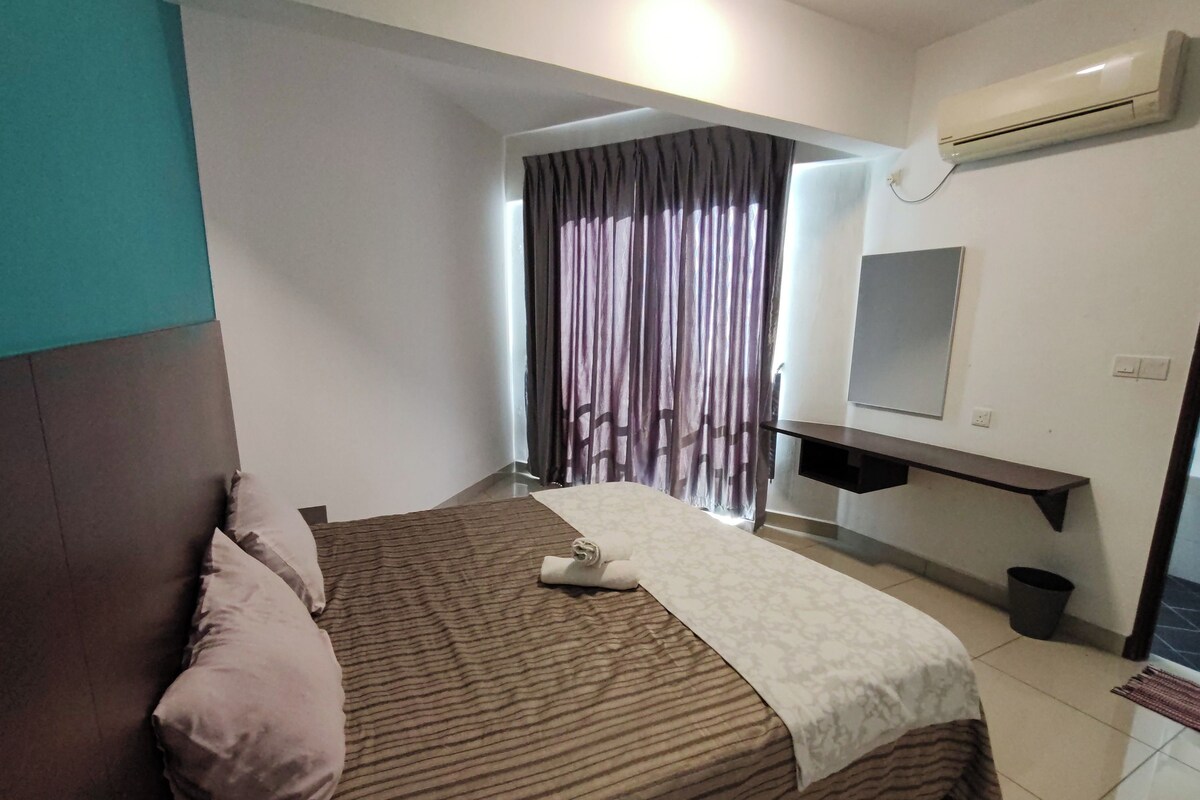 A hotel room with a bed, a bedside table, an air conditioner, a mirror, and a window with curtains.