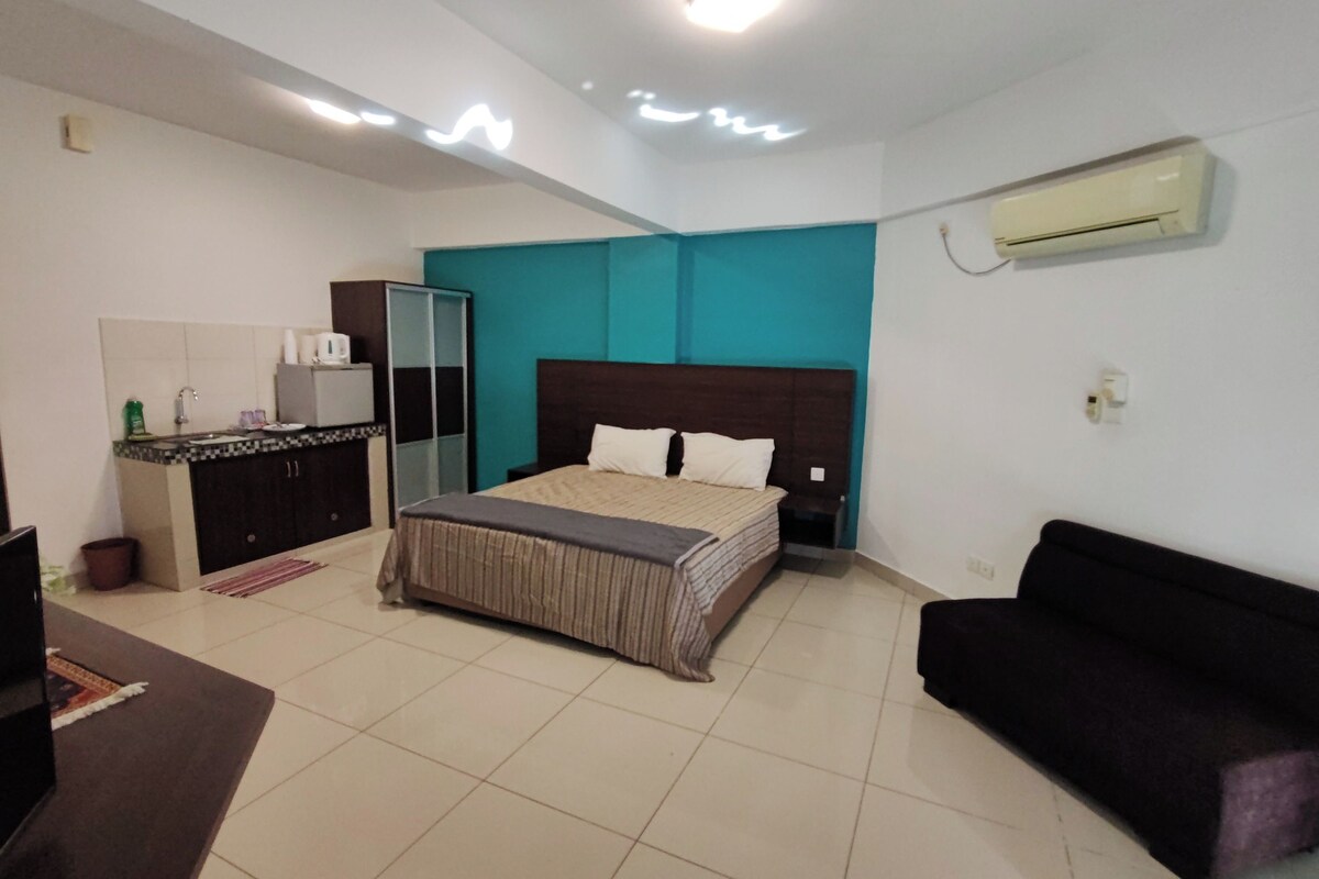 Quarto de hotel com cama, sofá, cozinha compacta e ar condicionado.