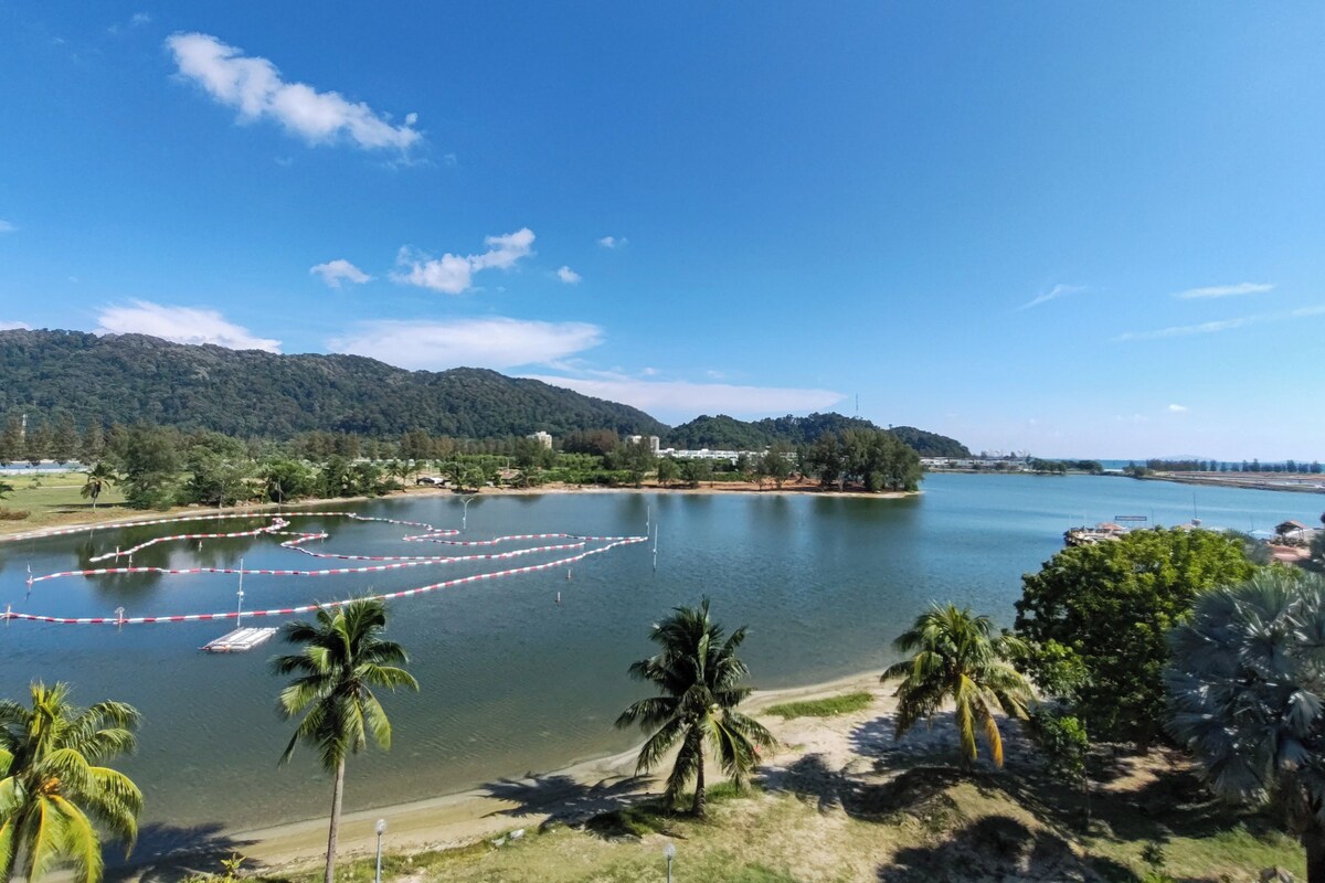 A coastal landscape with a clear sky, a body of water, and a beach with palm trees.