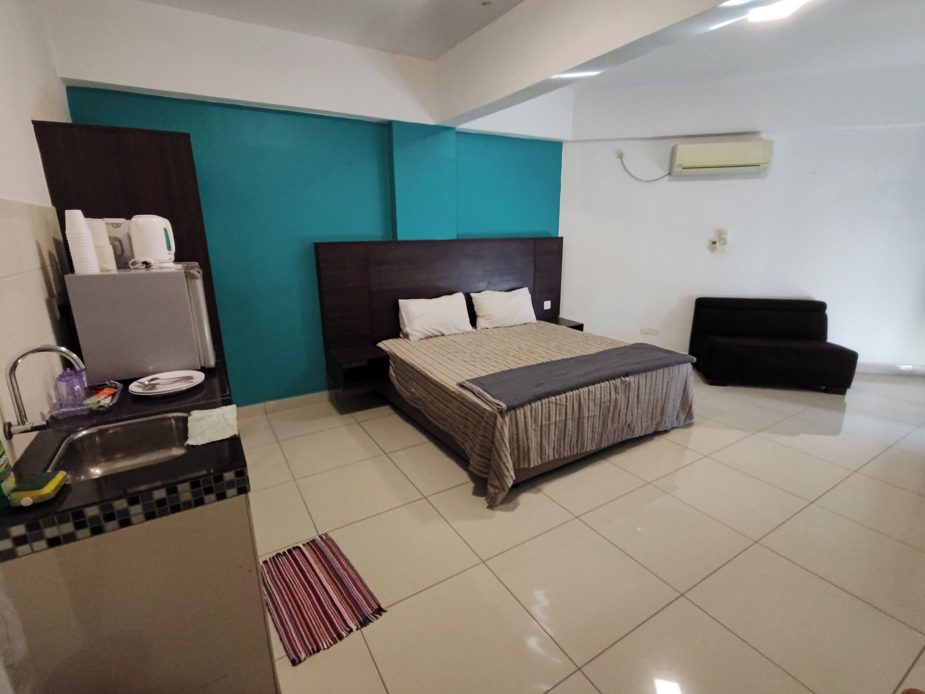 A hotel room with a bed, a small desk with a chair, a sink, and a mirror.