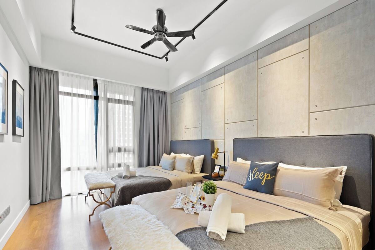 Ein modernes Hotelzimmer mit zwei Betten, einem Deckenventilator, einem großen Fenster mit Vorhängen und Holzboden.