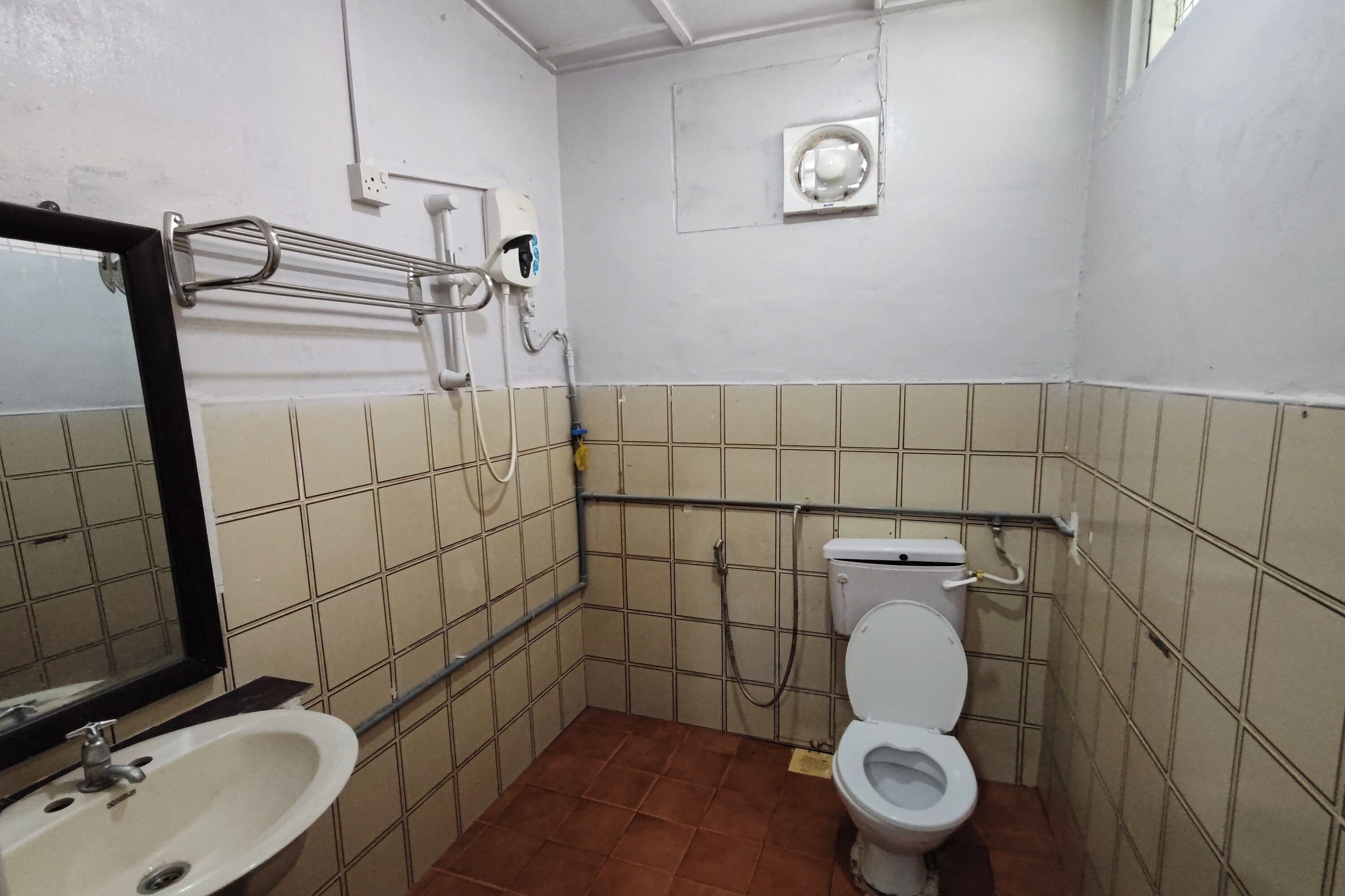 Et lille badeværelse med fliser, et håndvask, toilet og gelænder.