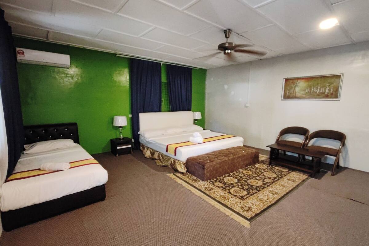 Une chambre d’hôtel avec deux lits, un ventilateur de plafond, un mur vert, un tapis à motifs et un tableau.