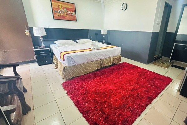 A hotel room with a bed, a red rug, a clock on the wall, and a painting above the bed. - Green Town Hotels And Resorts (Port Dickson)