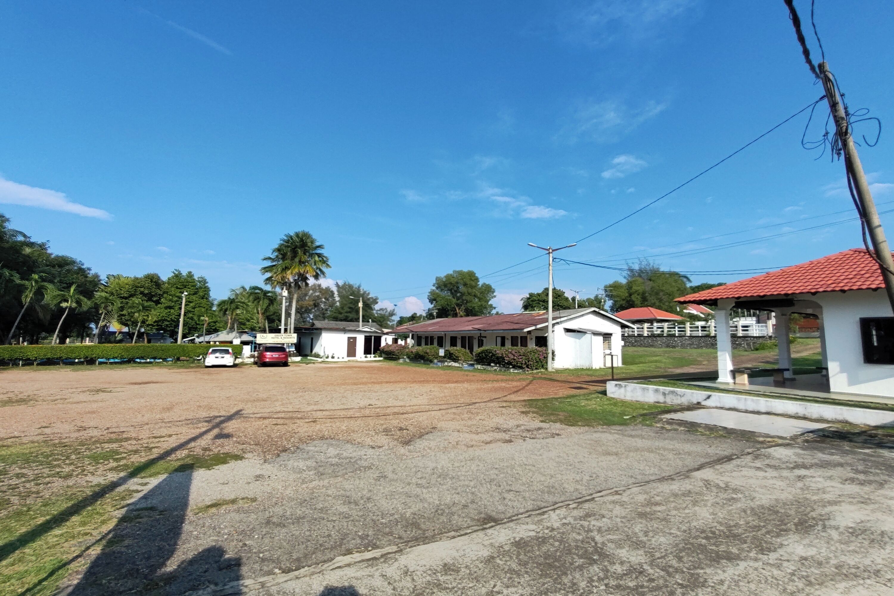 A spacious parking area with a few vehicles, surrounded by buildings with red roofs and a small white structure.
