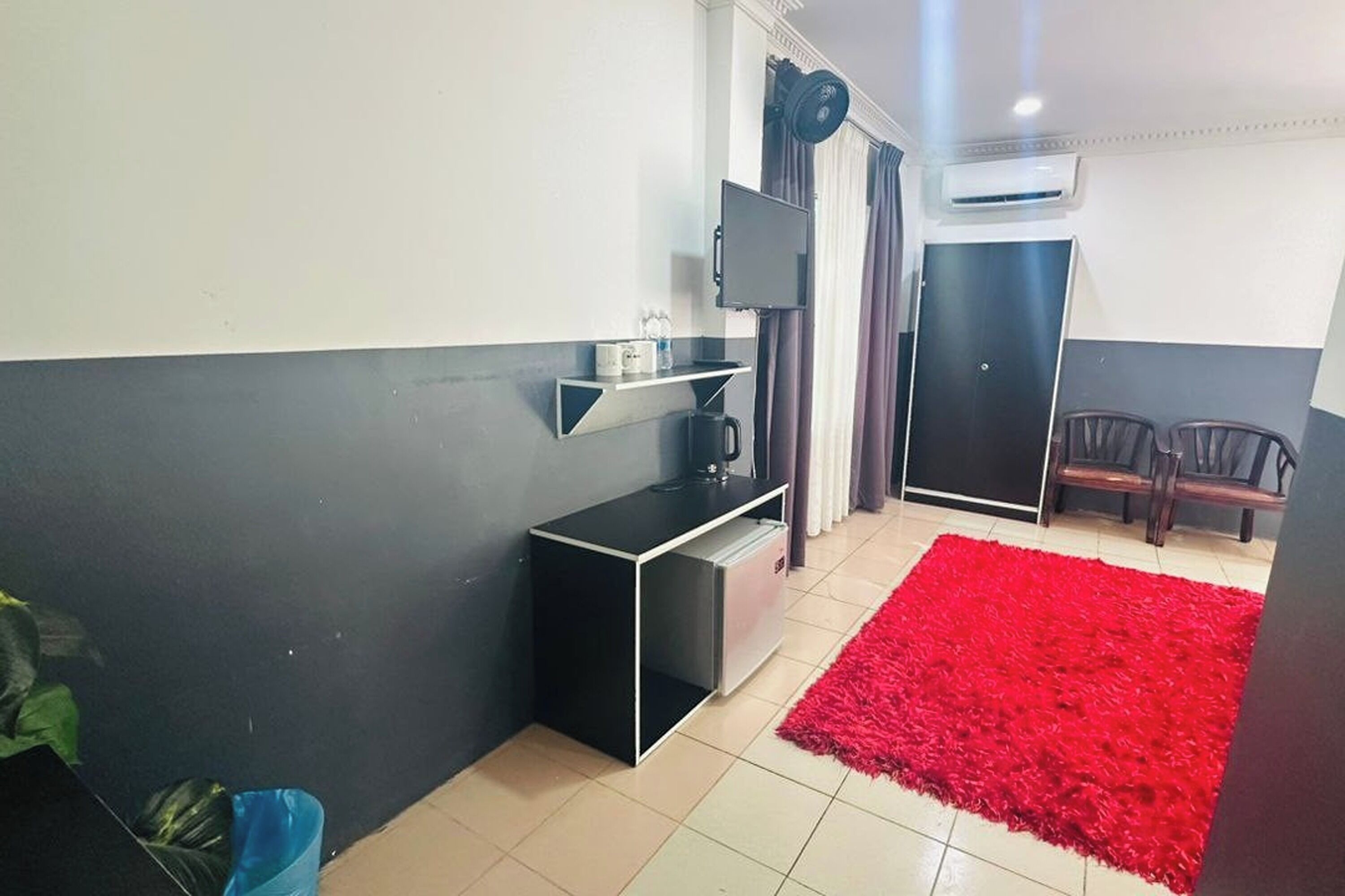 A compact hotel room with a black and white color scheme, a flat-screen TV mounted on the wall, a small black console table, a red shag rug, and a door with a dark frame.