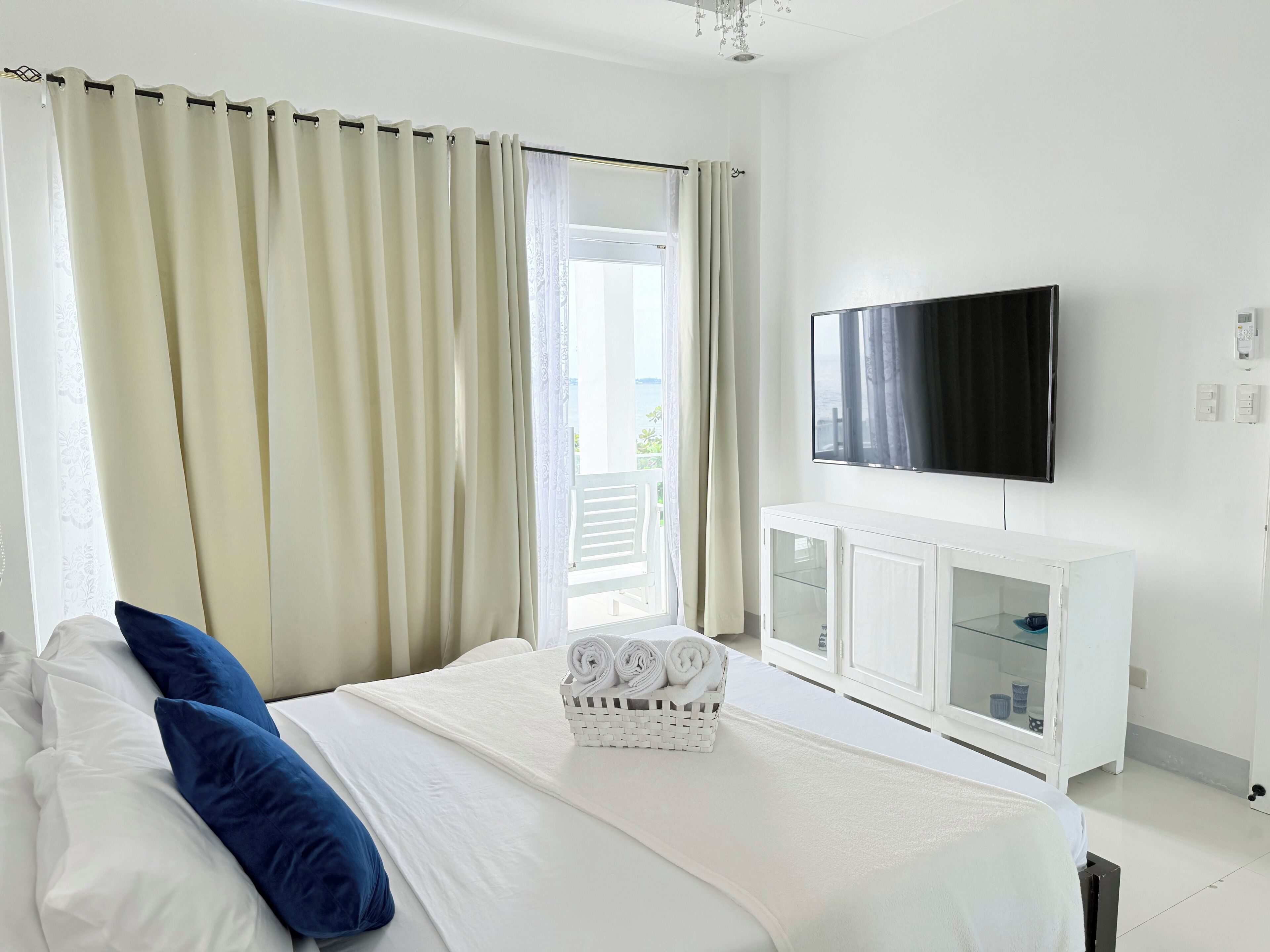 A hotel room with a bed, a television, a white cabinet, and a balcony with curtains.