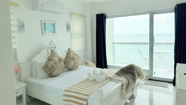 A bedroom with a bed, a window with a view of the sea, and a balcony with outdoor furniture. - Chateau Du Soleil (San Fernando)