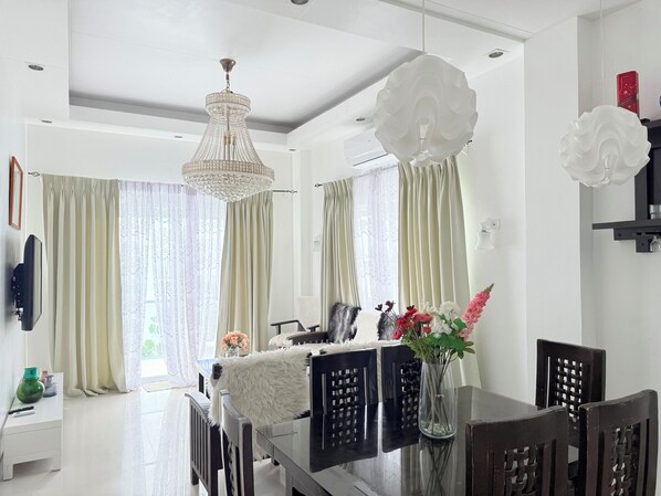 A modern dining area with a chandelier, dining table, chairs, and a vase with flowers. - Chateau Du Soleil (San Fernando)