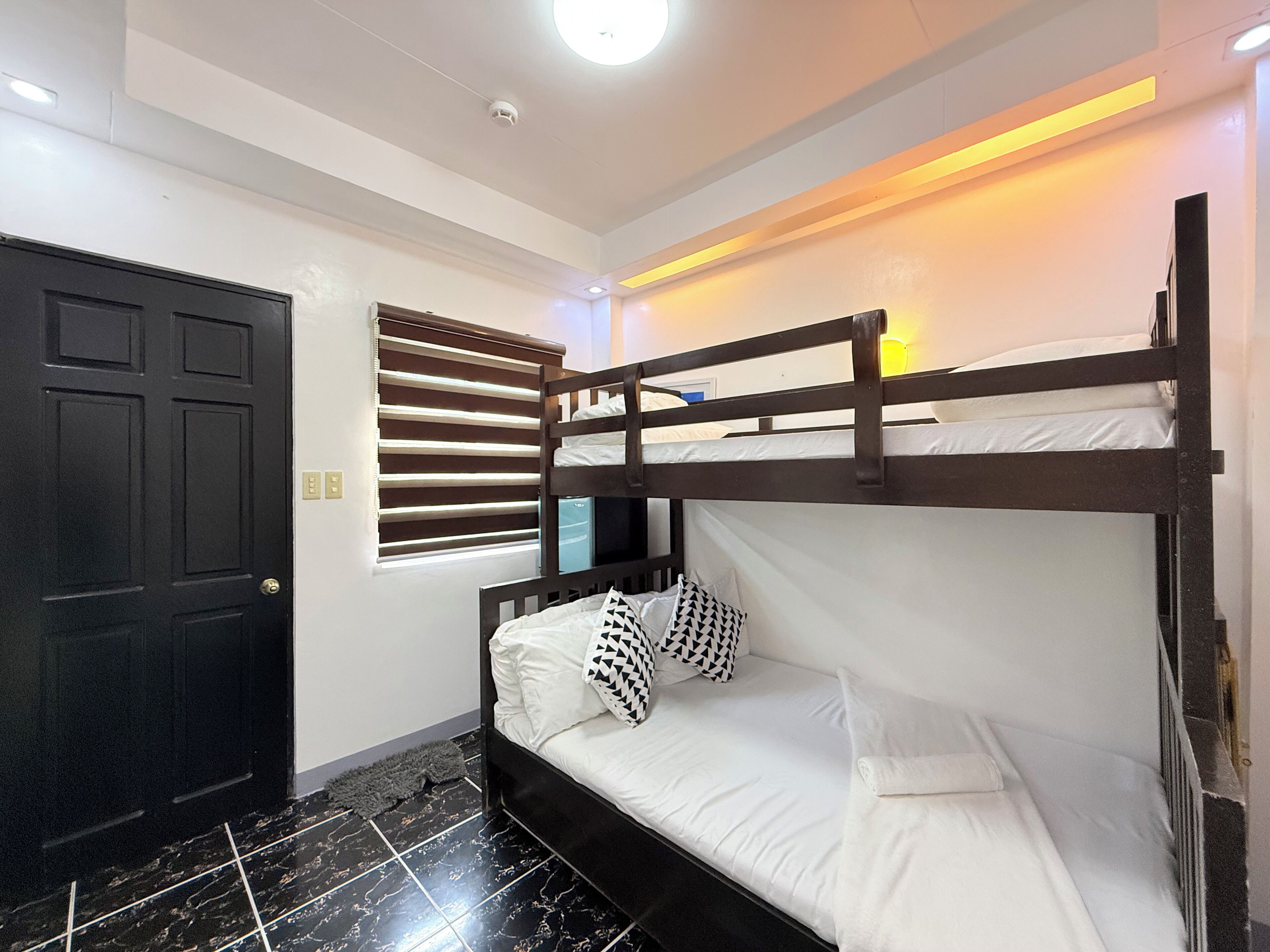 A bunk bed room with a black door, a window with blinds, and a ceiling light.
