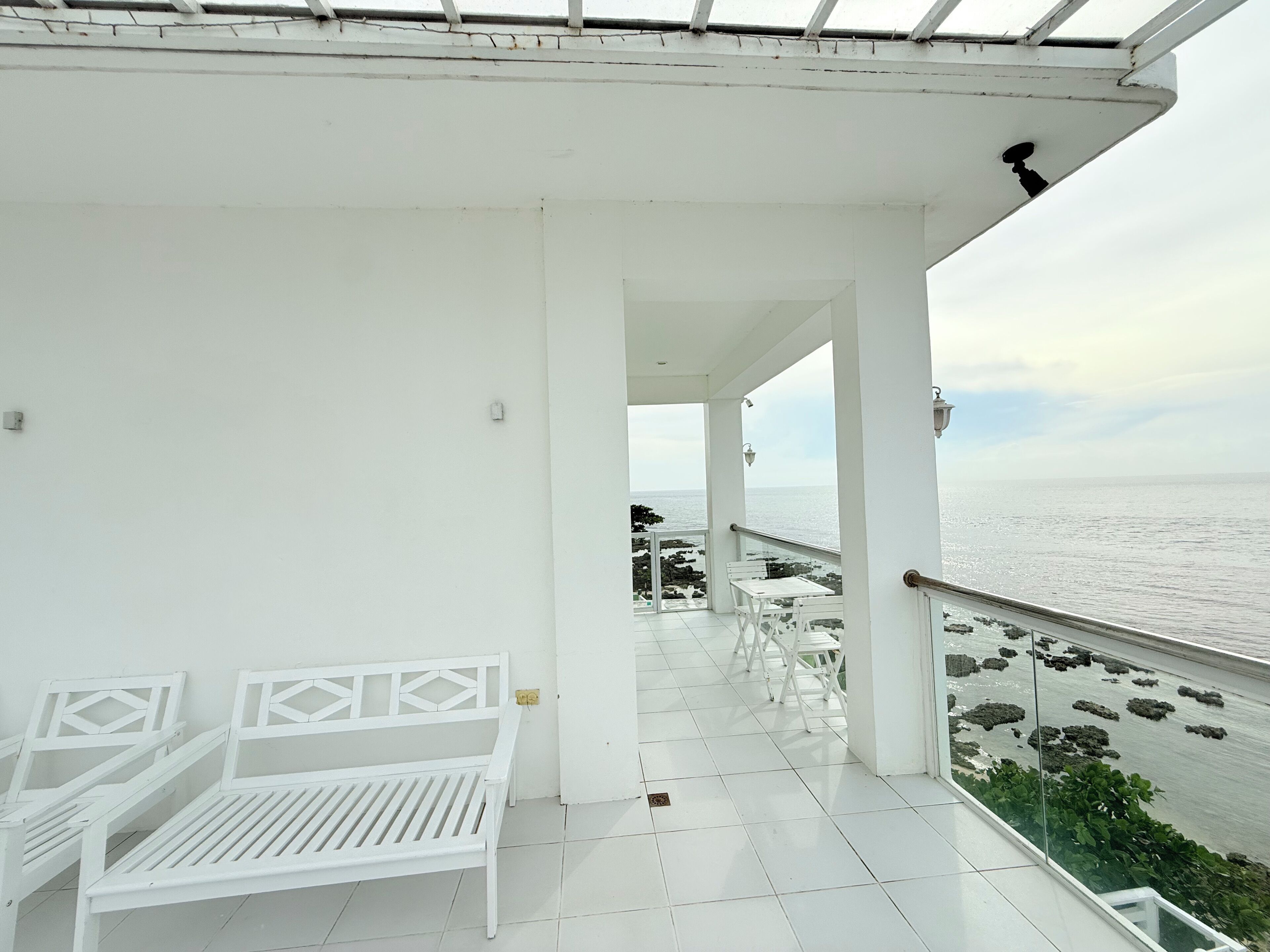 Un balcon blanc, agrémenté d’un banc et de tables, qui offre une vue sur une côte rocheuse.