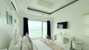 A modern bedroom with a large bed, a TV, and a view of the sea. - Chateau Du Soleil (San Fernando)