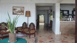 A spacious living area with a large plant, wooden chairs, a lamp, and a framed picture on the wall. - Hardin De Corales (San Fernando)