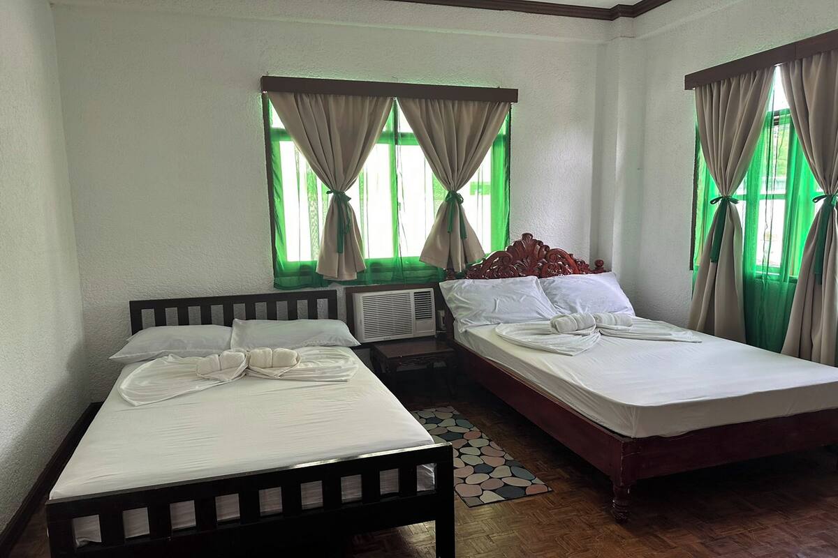 A hotel room with two beds, a wooden headboard, a small table, and a window with curtains.