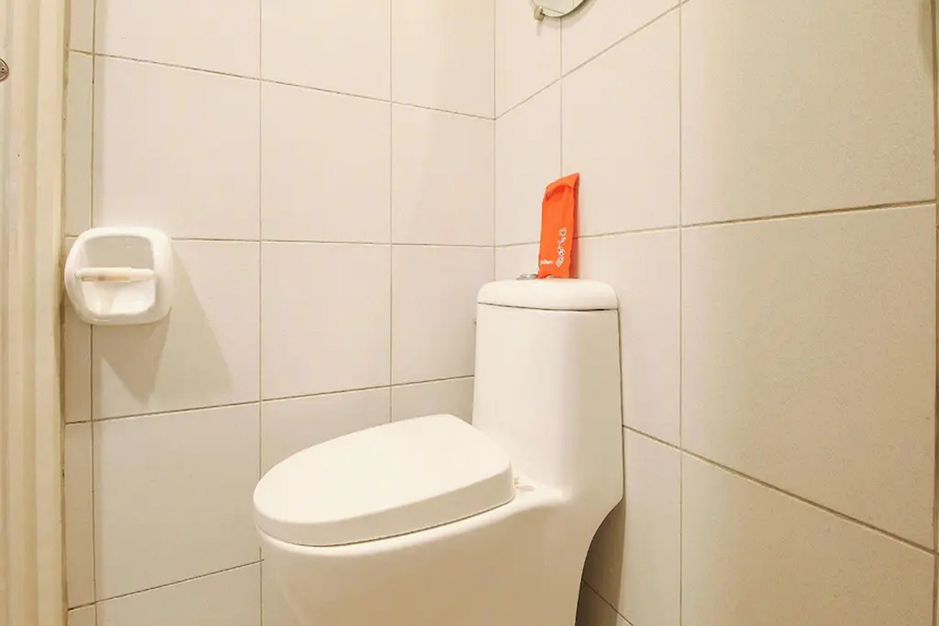 A white toilet with a tissue holder on the wall and a toilet paper dispenser to the left.