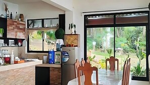 A modern kitchen with a dining area, large windows, and a view of greenery. - Hardin De Corales (San Fernando)