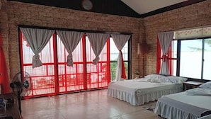 A hotel room with two beds, a fan, and a view through large windows with red curtains. - Hardin De Corales (San Fernando)