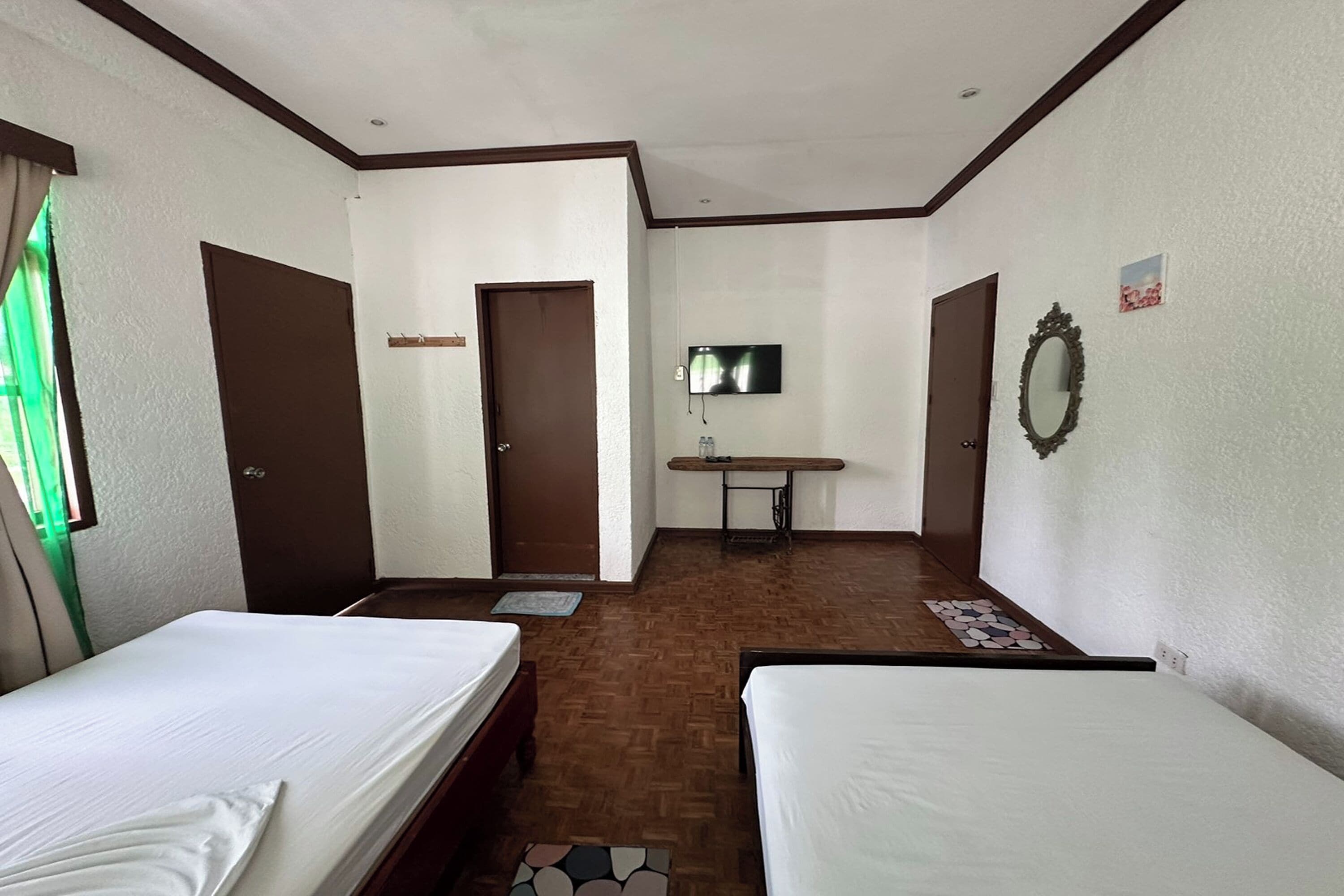 Habitación de hotel con dos camas, un televisor montado en la pared, un espejo y una mesita.