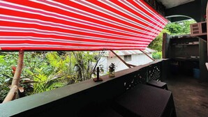 Ein Balkon mit einem rot-weiß gestreiften Jalousievorhang, einem kleinen Tisch und einem Stuhl.