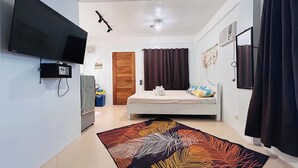 Ein Schlafzimmer mit einem Bett, einem Fernseher, einem Deckenventilator und einem Fenster mit Vorhängen.
