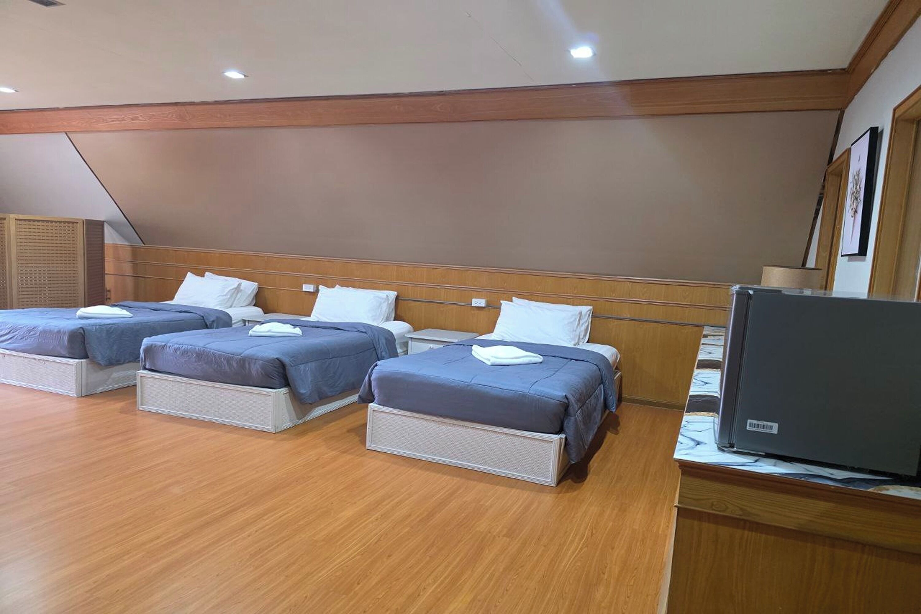 Une chambre d’hôtel avec trois lits, un plancher en bois, une télévision et une tête de lit en bois.