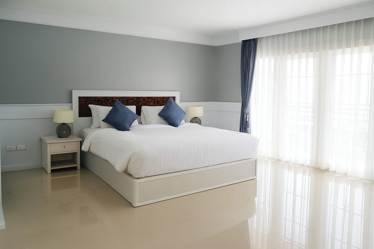 Un dormitorio moderno de hotel con una cama grande, dos mesitas de noche y vistas al exterior a través de cortinas translúcidas.