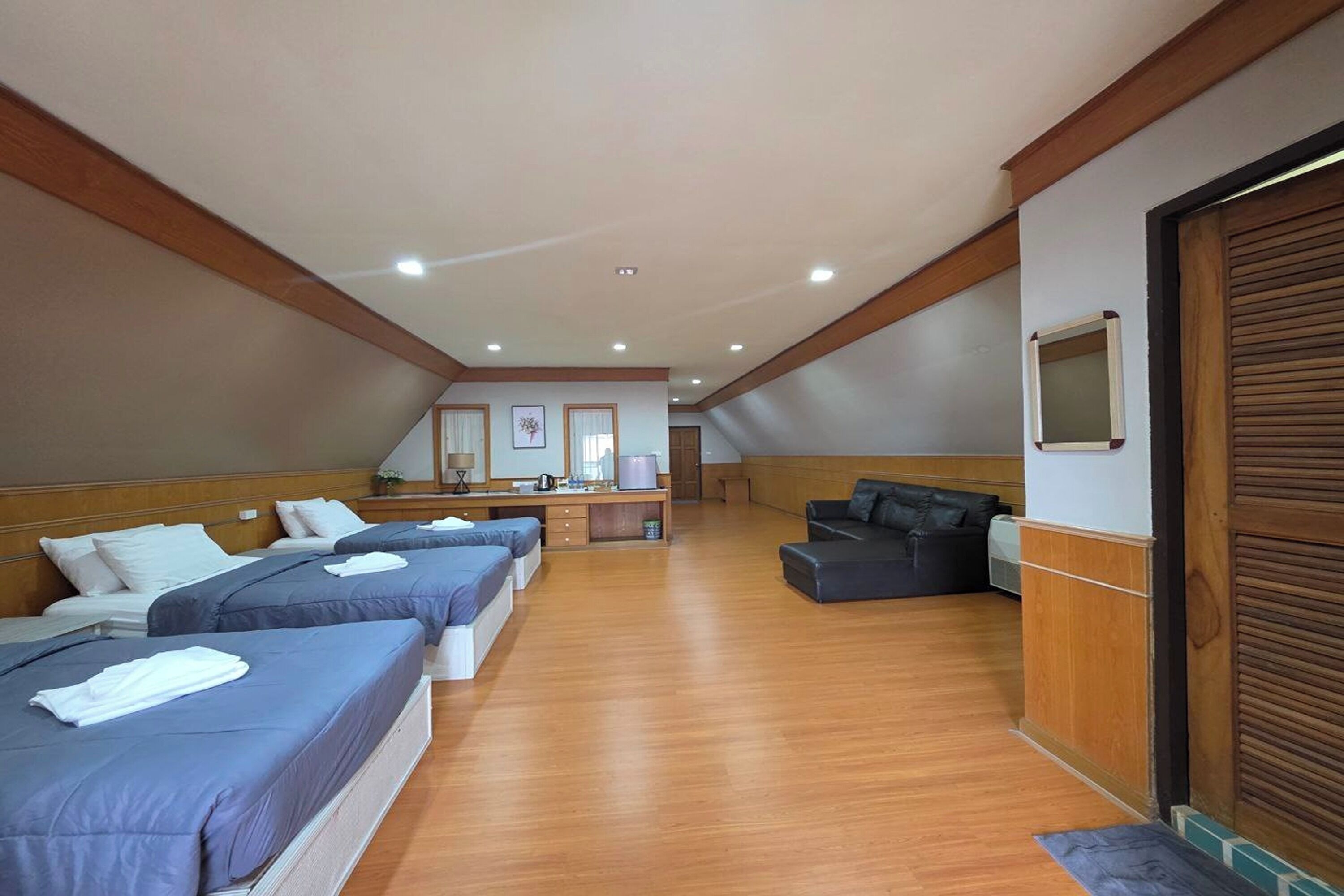 A hotel room with three beds, a desk, a sofa, and a kitchenette.