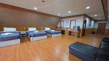 A hotel room with three beds, a desk, a sofa, and a kitchenette.