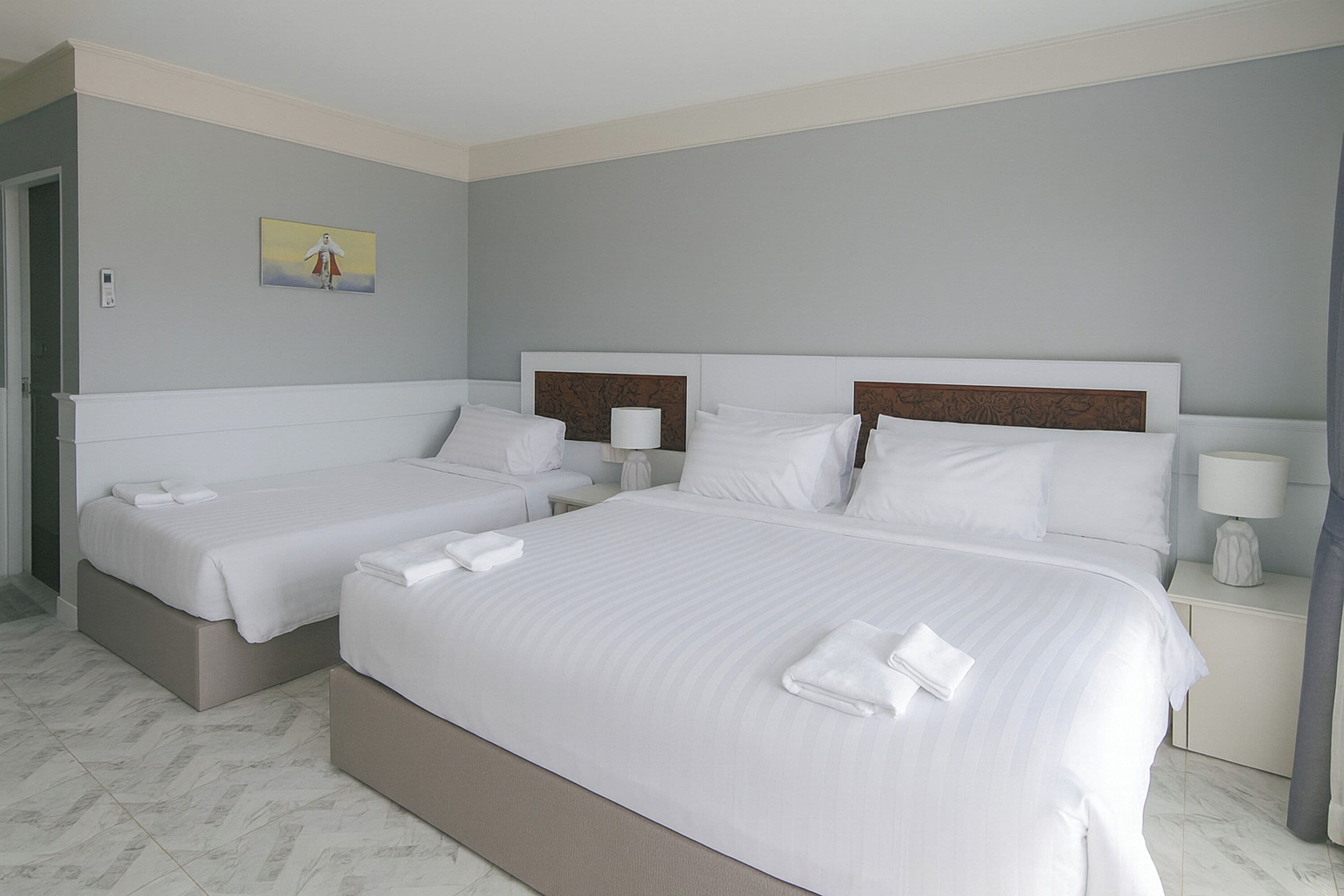 Habitación de hotel con dos camas, una mesita de noche con lámpara y un cuadro en la pared.