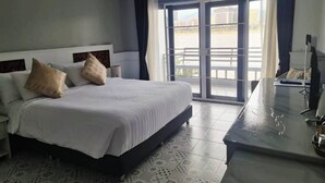 Ein Hotelzimmer mit einem großen Bett, einem Schreibtisch mit Stuhl und einem Balkon mit Stadtblick.