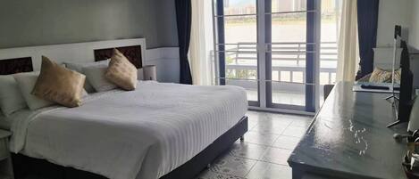 A hotel room with a large bed, a desk with a chair, and a balcony with a view of the city.