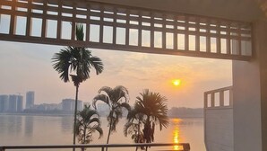 Ein Balkon mit Blick auf einen Sonnenuntergang über dem Wasser, Palmen und eine Stadtkulisse im Hintergrund.