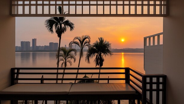 Ein Balkon mit Blick auf einen Sonnenuntergang über dem Wasser, Palmen und eine Stadtansicht in der Ferne.