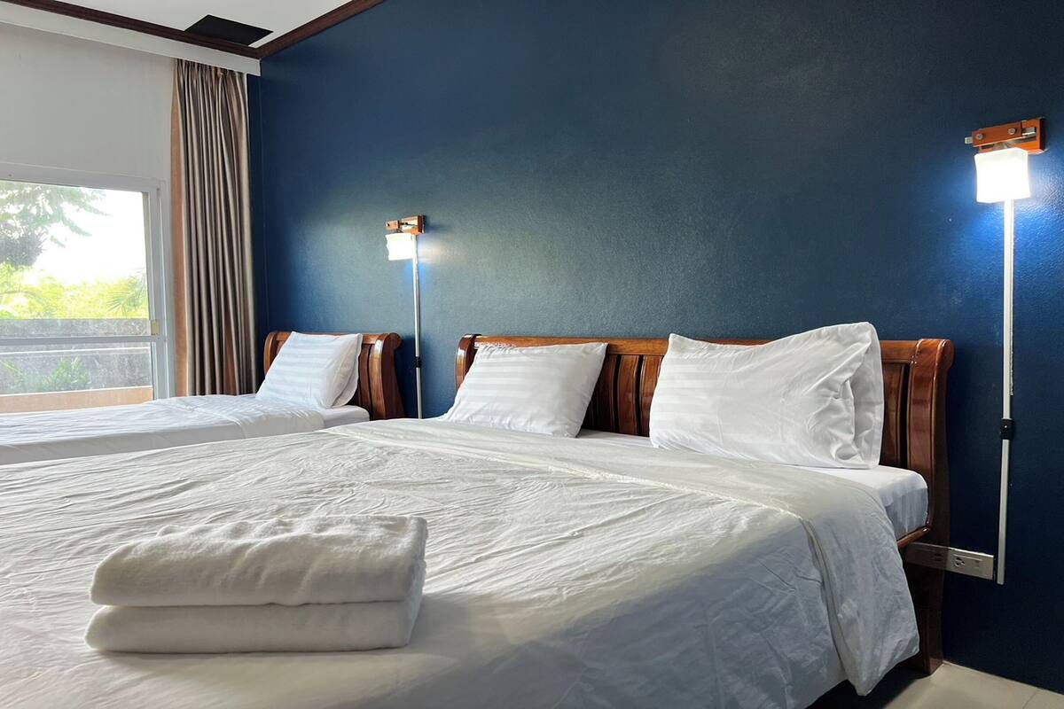A hotel room with two beds, a large window with curtains, and two wall-mounted lights.
