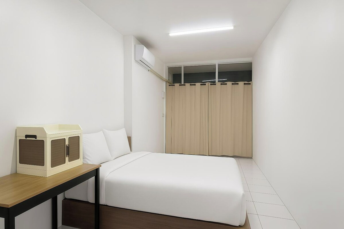 Une petite chambre à coucher, bien rangée, avec un lit simple, une table de chevet en bois, une armoire et un appareil de climatisation fixé au plafond.