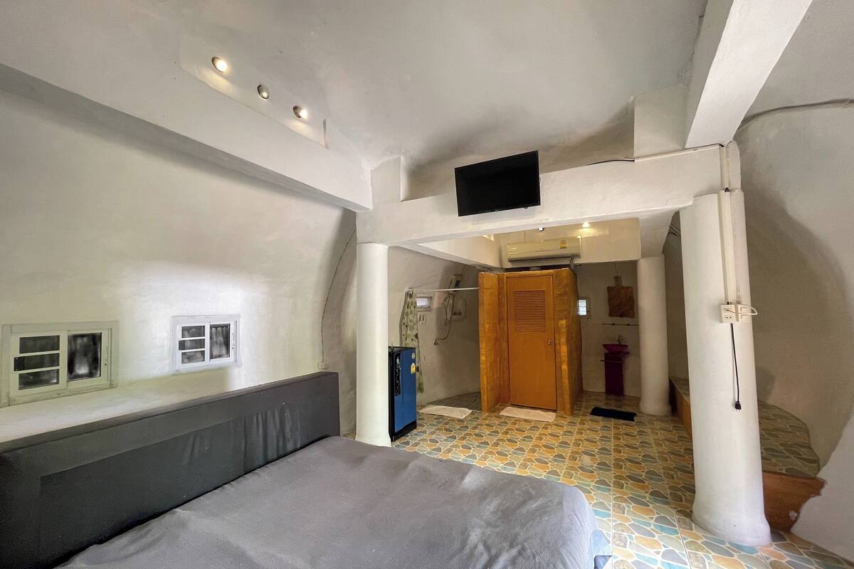 Une chambre à coucher avec un lit, un téléviseur fixé au mur, une salle de bain avec douche et un sol carrelé.