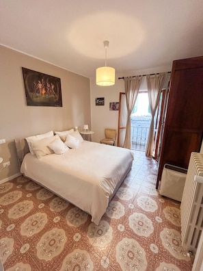 Ein Schlafzimmer mit Bett, Sessel, Tisch, einem Bild an der Wand und Blick durch das Fenster.