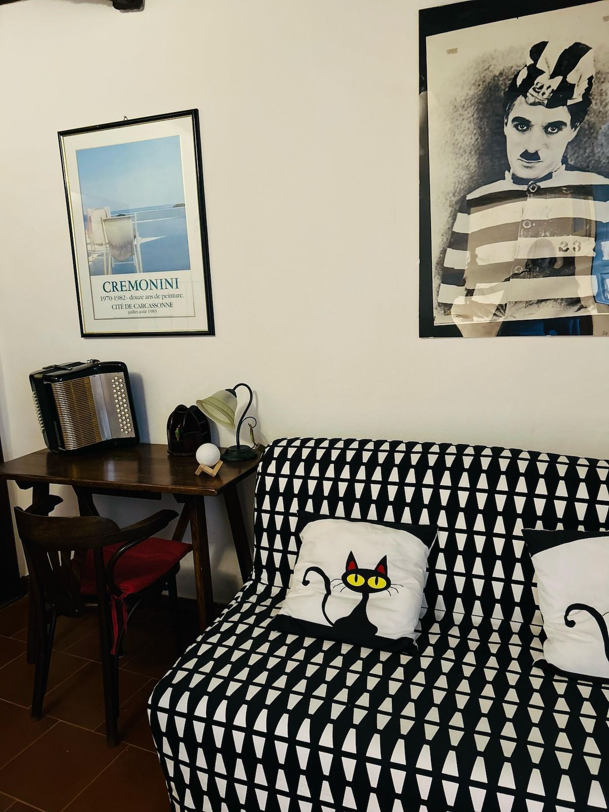 A room with a patterned sofa, a framed picture on the wall, a table with a radio, and a chair.
