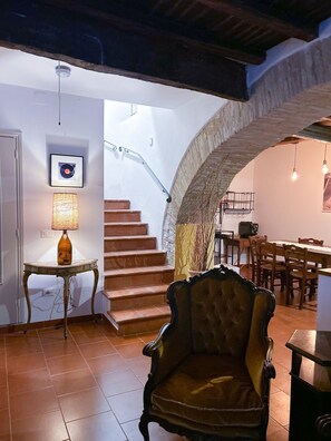 Ein Zimmer mit einer Treppe zu einer oberen Ebene, einem Essbereich mit Holzmöbeln und einem alten Sessel.