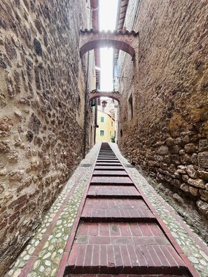 A narrow alleyway with stone walls and a brick pathway leading to a building with a tiled roof.