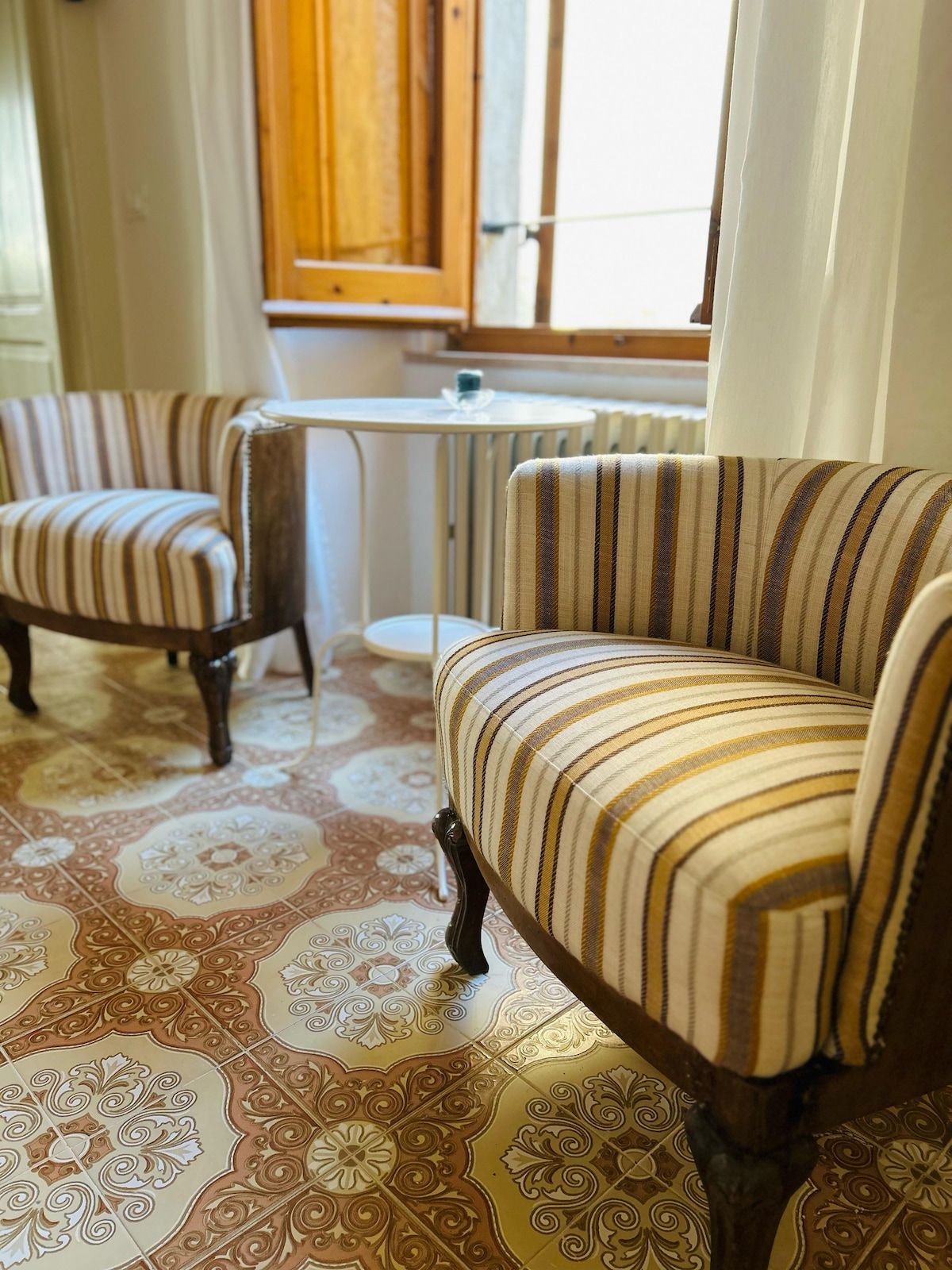 Ein Zimmer mit zwei gestreiften Sesseln, einem kleinen runden Tisch und einer Heizung.
