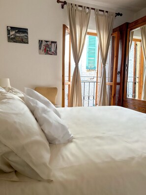 A bedroom with a bed, a chair, and a balcony with curtains.